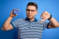 Young man with blue eyes wearing glasses and holding credit card over blue background with angry face, negative sign showing Royalty Free Stock Photo