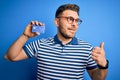 Young man with blue eyes wearing glasses and holding credit card over blue background pointing and showing with thumb up to the Royalty Free Stock Photo