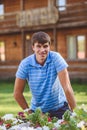 A young man in a blue shirt and blue shorts near decorative wooden carts with flowers, on a background of rustic style