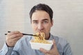 young man in a blue shirt is eating noodles from a box with a dissatisfied face. Lunch at the office. tasteless junk Royalty Free Stock Photo