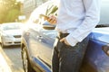 Successfull happy young man and his car in soft sunset light on urbanistic background. Busines man with vehicle on roadside. Royalty Free Stock Photo