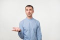 Young man in blue shirt standing disorientated bewildered on gray wall background. Decision making concept.