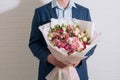 Young man in a blue suit holds in hand a big bouquet of white-pink roses and eustoma in pink packaging on the white wall Royalty Free Stock Photo