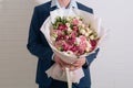 Young man in a blue suit holds in hand a big bouquet of white-pink roses and eustoma in pink packaging on the white wall Royalty Free Stock Photo