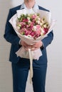 Young man in a blue suit holds in hand a big bouquet of white-pink roses and eustoma in pink packaging on the white wall Royalty Free Stock Photo