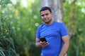 Young man in blue t shirt standing with tree using cellphone outdoor in park Royalty Free Stock Photo