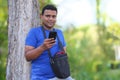 Young man in blue t shirt standing with tree using cellphone outdoor in park Royalty Free Stock Photo