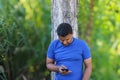 Young man in blue t shirt standing with tree using cellphone outdoor in park Royalty Free Stock Photo