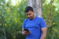 Young man in blue t shirt standing with tree using cellphone outdoor in park Royalty Free Stock Photo