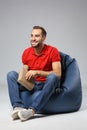 Young man with book sitting on beanbag chair against grey background Royalty Free Stock Photo