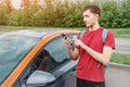 Man books a car or taxi on a smartphone in the carsharing app to get around the city. New generation chooses not to own a