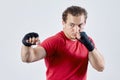 Young man boxes, making hook with right hand. Black bandages, red T-shirt, determined face expression, strong emotions. Royalty Free Stock Photo