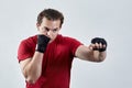 Young man boxes, making jab with left hand. Black bandages, red T-shirt, determined face expression, strong emotions. Royalty Free Stock Photo