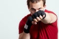 Young man boxes, making jab with left hand. Black bandages, red T-shirt, determined face expression, strong emotions.