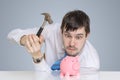 Young man is breaking piggy money bank with hammer to take his savings