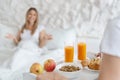 Young man bringing tasty breakfast to bed for his beloved woman, focus on tray with juice, cereals and croissants Royalty Free Stock Photo