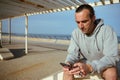 Young man browsing fitness app on mobile phone, scrolling newsfeed, checking social media content in Atlantic promenade