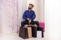 Young man with a bunch of bags is sitting in the fitting room and waiting. the girl in the dressing room tries on outfits, the guy Royalty Free Stock Photo