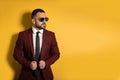 Young man in burgundy suit looking seriously sideways wearing sunglasses with hands holding a jacket isolated on yellow Royalty Free Stock Photo