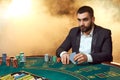 A young man in a business suit sitting at the poker table. Man gambles. The player at the gaming table playing cards.