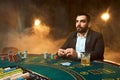 A young man in a business suit sitting at the poker table. Man gambles. The player at the gaming table playing cards. Royalty Free Stock Photo