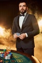 A young man in a business suit standing near poker table. Man gambles.