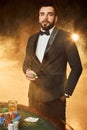 A young man in a business suit standing near poker table. Man gambles.