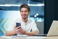 Young man, businessman, manager sitting in the office at his desk, holding a mobile phone, typing messages, making phone calls. Royalty Free Stock Photo