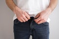 Young man buttoning jeans on gray background, close-up