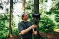 A young man with a camera on a stabilizer stands in the woods and creates travel content on a hike. Guy holds a gimbal with a