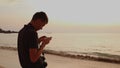 Young man with a camera stands on the beach and shoots video on a smartphone