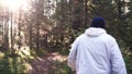 Young man on camping trip. Concept of freedom and nature. View of man from back walking in woods along path on sunny