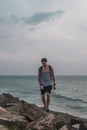 Young man in cap, t-shirt and shorts walks on stones by the sea