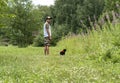 Young man in cap walking with black cat in red harness on leash on green grass, friendship pet love and care Royalty Free Stock Photo