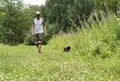 Young man in cap walking with black cat in red harness on leash on green grass, friendship pet love and care Royalty Free Stock Photo