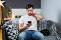 Young man after car accident suffering at home. Male in foam cervical collar reading message on cellphone, feeling pain in neck. Royalty Free Stock Photo