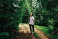 A young man in casual clothes and with a bag on his shoulder stands on a mountain road and looks away at the pine trees. Tourists