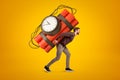 Young man in casual clothes carrying big red dynamite stick time bomb on his back on yellow background Royalty Free Stock Photo