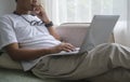 Young man in casual clothes surfing internet on laptop computer while sitting on couch at home Royalty Free Stock Photo