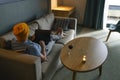 Young man in casual clothes and yellow hat sits with laptop and red wine glass in the cozy living room on sofa Royalty Free Stock Photo