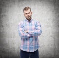 Young man in casual shirt with crossed hands. Concrete wall.