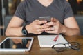 Young man in casual using smartphone, digital tablet and notebook at cafe.