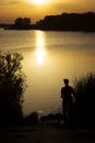 A young man catches fish in the lake at sunset. Beautiful sun reflection on the water. Relaxation Royalty Free Stock Photo