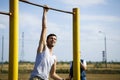 A young man of Caucasian appearance pulls himself up on a horizontal bar.