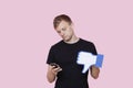 Young man with cell phone holding fake dislike button against pink background