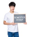 Young man with chalkboard showing phrases of semester start Royalty Free Stock Photo