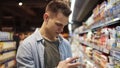 Young man chooses jogurt or sour cream in the supermarket, customer selects product on the milk products shelves in the