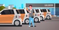 Young man choosing vehicle on car center parking using mobile application carsharing concept guy holding smartphone