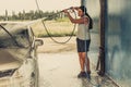 Young man cleaning his car using high pressure water in self-service car wash Royalty Free Stock Photo