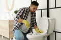 Young man cleaning toilet bowl in bathroom Royalty Free Stock Photo